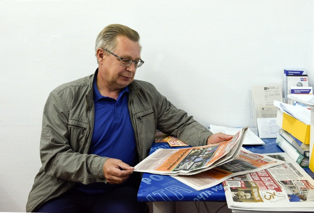 Фото взрослого мужчины, читающего газету, на фоне текстов и публикаций.