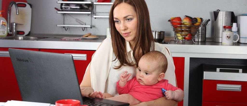 Фотография человека, работающего на ноутбуке в кухне, рядом с ребенком.